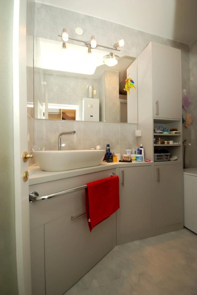 Modern bathroom vanity with round vessel sink, lighted mirror, red hand towel, and wall-mounted shelving with toiletries