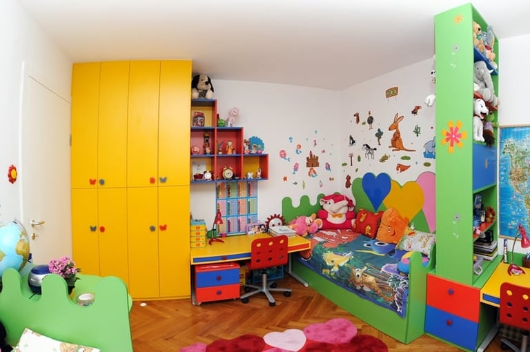 Colorful childrens bedroom with yellow wardrobe, green shelving, red desk, and playful wall decorations